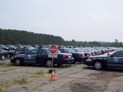 1991 Ford LTD Crown Victoria - A large lot filled with numerous parked police vehicles, some with light bars visible.