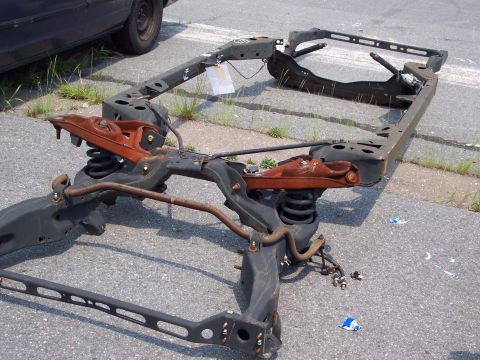 1991 Ford LTD Crown Victoria - A car frame, likely from a sedan, sits on asphalt with visible suspension components and signs of rust.
