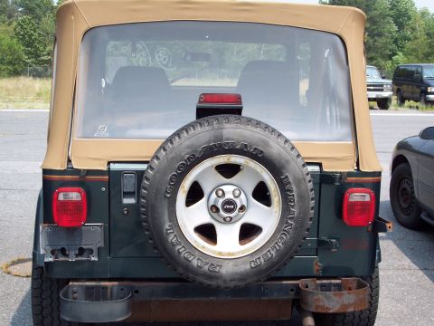 1991 Ford LTD Crown Victoria - Dark green Jeep Wrangler rear view, a spare tire and tan soft top. Another vehicle is parked nearby.