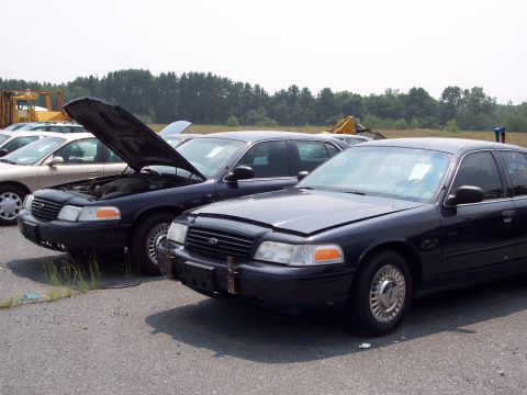1991 Ford LTD Crown Victoria - Two Ford Crown Victoria police cars are parked side-by-side in an outdoor lot.