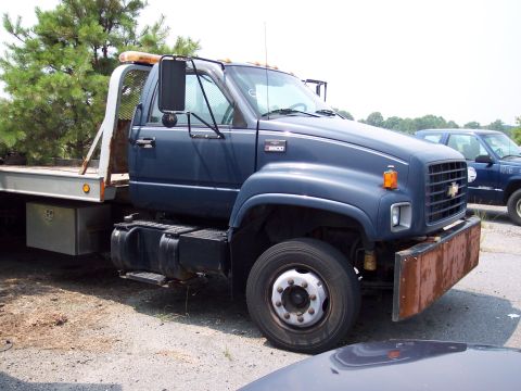 1991 Ford LTD Crown Victoria - A dark blue tow truck is parked outdoors, with a flatbed and a rusty front bumper visible. Another vehicle is parked behind it.