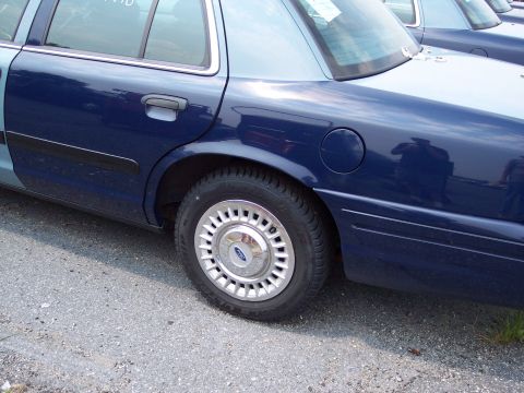 1991 Ford LTD Crown Victoria - Side view of a blue Ford Crown Victoria, showing the rear wheel and fuel door. Another vehicle is parked behind it.