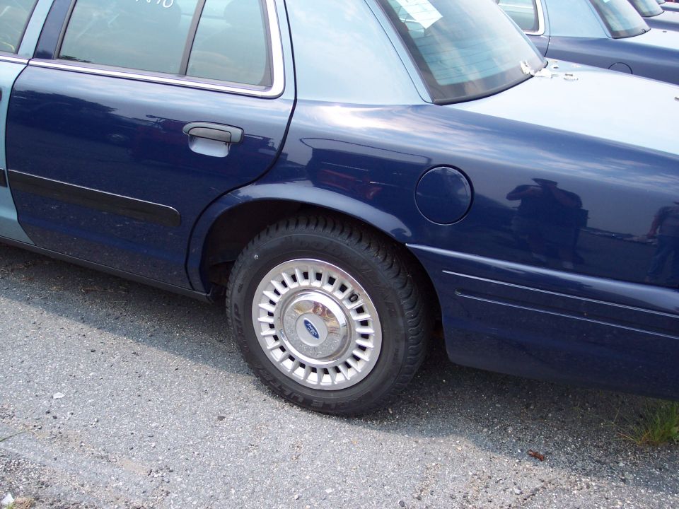 Rear quarter panel and wheel of a blue Ford Crown Victoria. Another similar car is visible behind it