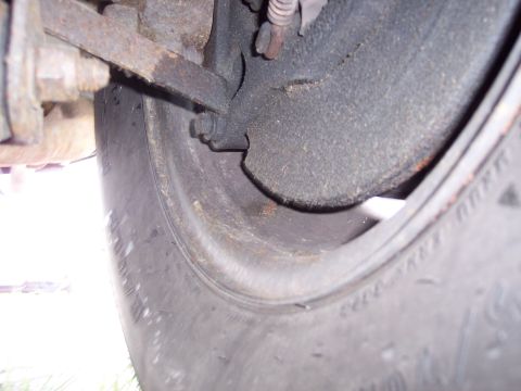 1991 Ford LTD Crown Victoria - Detail of a vehicle's undercarriage, showing a rusty suspension part and brake drum assembly.