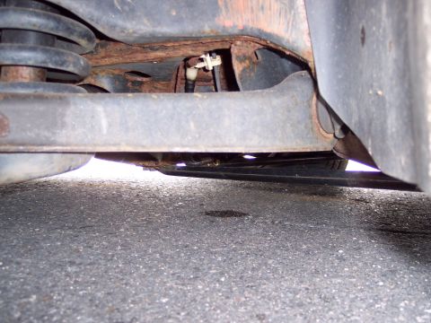 1991 Ford LTD Crown Victoria - Vehicle underbody shows significant rust and suspension parts, with a dark fluid stain on the asphalt.
