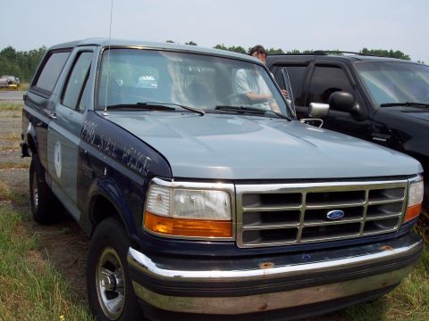 1991 Ford LTD Crown Victoria - This Ford Bronco, marked 'STATE POLICE', is parked next to another dark SUV under a cloudy sky.
