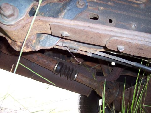1991 Ford LTD Crown Victoria - The heavily rusted underbody of a vehicle shows signs of wear and tear, with various mechanical parts obscured by grass.