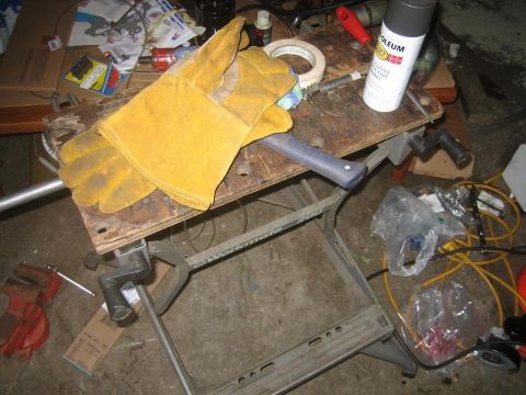 1969 Ford Mustang - A workbench scene yellow work gloves, tape, and a can of spray paint, with various tools and materials scattered around.
