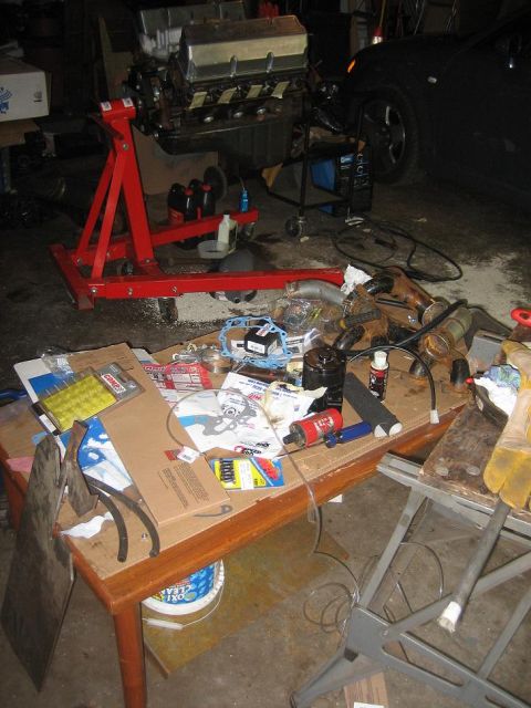 1969 Ford Mustang - Engine on stand with parts laid out on a table, garage setting with a car in the background.