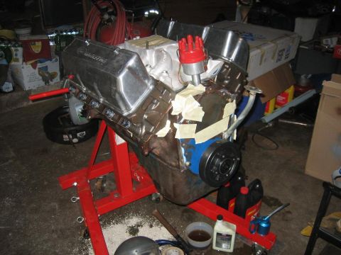 1969 Ford Mustang - A V8 engine is mounted on a red engine stand in a cluttered garage setting.