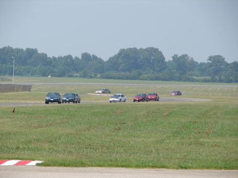 1992 Ford Taurus - Multiple sedans compete on a race track under a hazy sky, with a wooded area visible beyond the course.