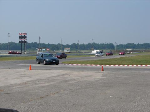 1992 Ford Taurus - Several cars are on a race track during a sunny day, with trees and a scoreboard in the distance.