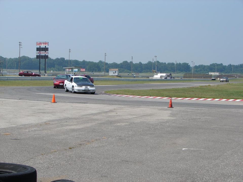 White sedan with a black hood on a race track, with other cars visible