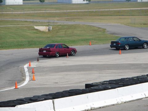 1992 Ford Taurus - Two sedans, one a 1992 Ford Taurus, navigate a race track with orange cones marking the course.