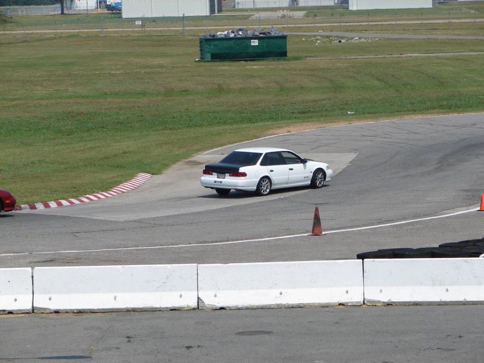 White sedan with black trunk on a race track, another red car visible on the left