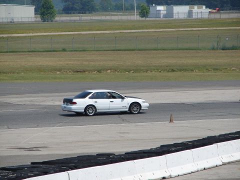 1992 Ford Taurus - A white 1992 Ford Taurus sedan with a black hood and trunk drives on a race track.