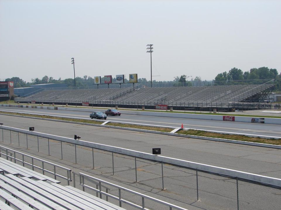 Two cars on a drag strip with grandstands in the background