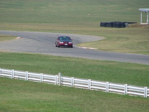 1992 Ford Taurus - A red 1992 Ford Taurus sedan navigates a turn on a race track during a sunny day.