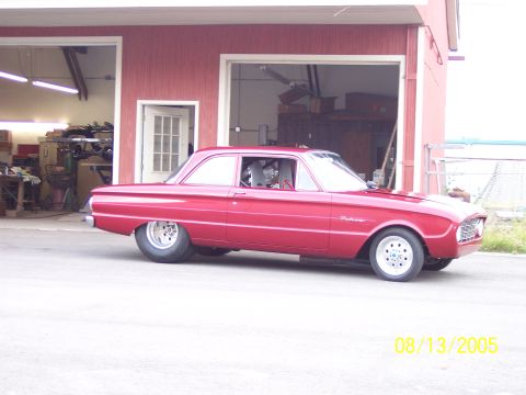 1960 Ford Falcon - A red 1960 Ford Falcon is parked outside a garage, showing its racing interior and custom wheels.