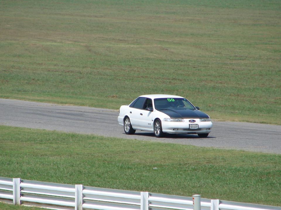 1992 Ford Taurus with black hood on a racetrack, number 59 on windshield