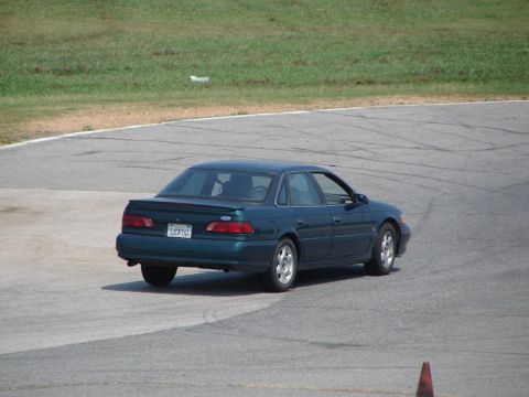 1992 Ford Taurus - A dark green 1992 Ford Taurus is seen from the rear on a race track.