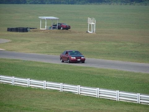 1992 Ford Taurus - A red 1992 Ford Taurus drives on a race track, with another car visible in the background.