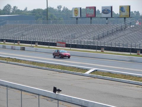 1992 Ford Taurus - A red sedan is on the drag strip with empty bleachers and billboards visible.