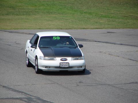 1992 Ford Taurus - A white 1992 Ford Taurus with a black hood is on a race track, displaying the number 59 on its windshield.
