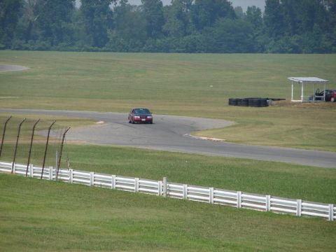 1992 Ford Taurus - A red sedan navigates a turn on a race track, with trees and a white fence in the background.