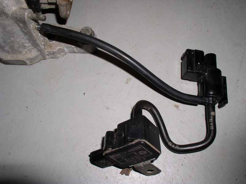 Engine part with two black plastic solenoids and black hoses connected to a metal manifold
