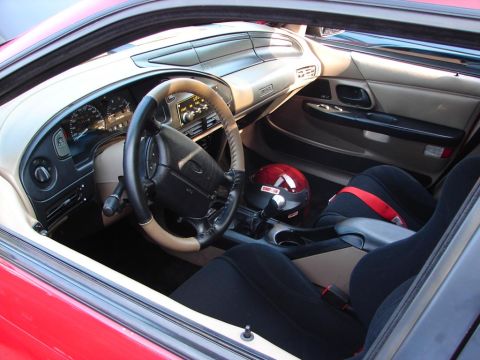 1992 Ford Taurus - The interior of a red car, likely a 1992 Ford Taurus, is visible with racing seats and a helmet.