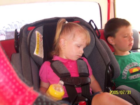 1985 Ford Bronco - Two young children are asleep in car seats inside a vehicle.