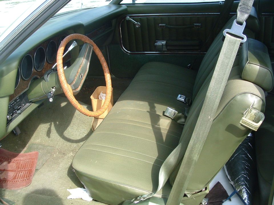 Interior of a car with green seats, dashboard, and steering wheel. A paper bag is on the floor