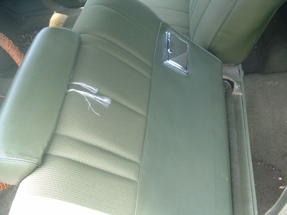 Green car interior showing a torn seat cushion and armrest with a chrome pull handle