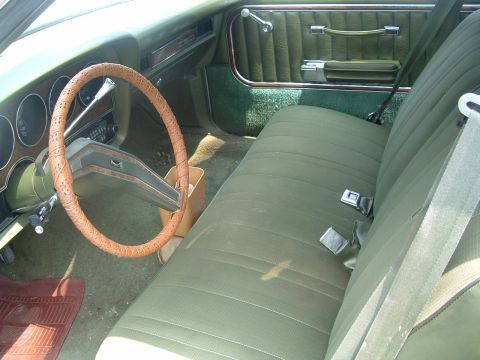 1975 Ford Torino - The interior of a classic car shows green upholstery, a wood-grain dashboard, and a distinctive steering wheel cover.