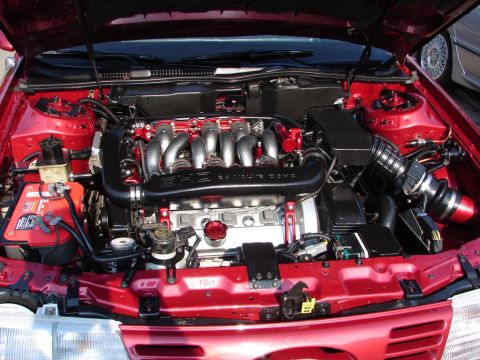 1992 Ford Taurus - The engine bay of a red 1992 Ford Taurus is shown with a V8 engine and aftermarket modifications.