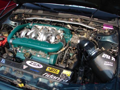 1992 Ford Taurus - The engine bay features a custom teal V6 engine with aftermarket parts and numerous stickers.