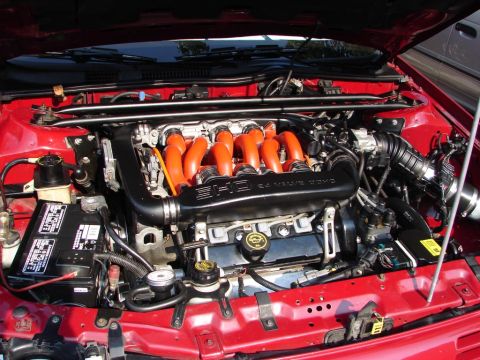 1992 Ford Taurus - The engine bay of a red 1992 Ford Taurus is visible, orange intake runners and a "32 Valve DOHC" cover.
