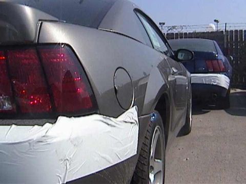 1989 Ford Mustang - Rear view of a gray Ford Mustang with protective wrap on the bumper and fender, with a blue Mustang behind it.