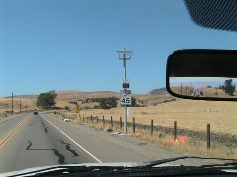 1971 Ford Bronco - Speed limit sign on a rural road with dry, rolling hills under a clear blue sky.