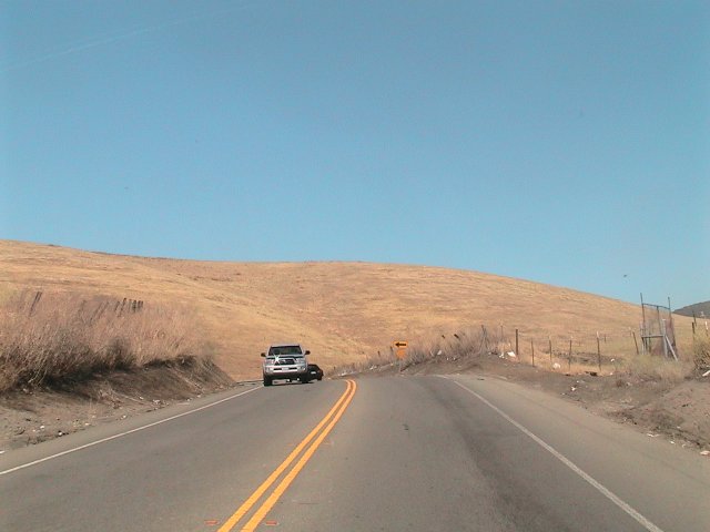 White pickup truck on a two-lane road, with a dark car behind it