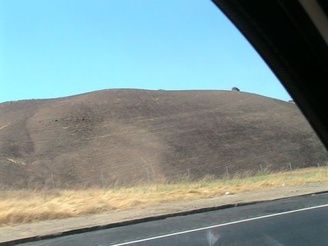 1971 Ford Bronco - A lone vehicle is visible on a distant hill, set against a backdrop of dry grass and a clear blue sky.