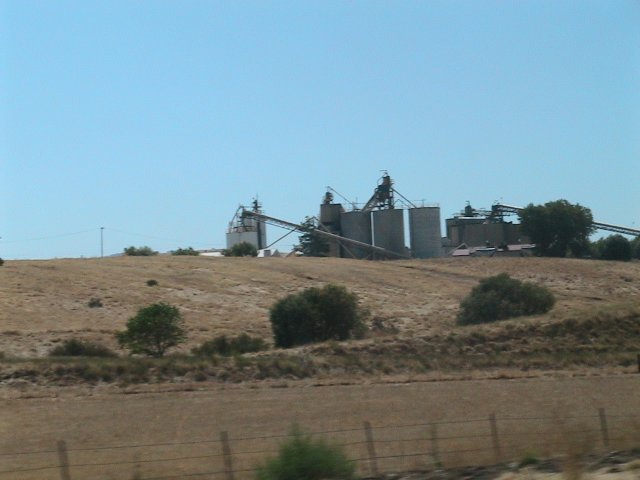 Industrial grain silos on a dry, grassy hill under a clear blue sky