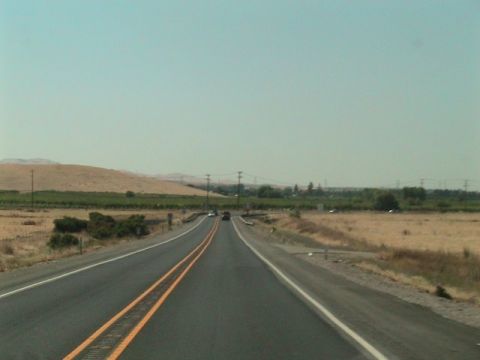 1971 Ford Bronco - A long, straight highway stretches through a dry, rural landscape under a hazy sky, with a few cars visible in the distance.