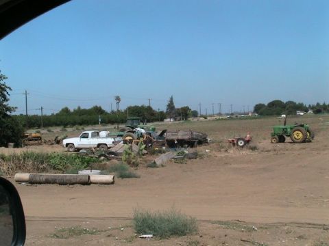 1971 Ford Bronco - A collection of farm vehicles, including a white pickup truck and multiple tractors, are parked in an open, dusty field.
