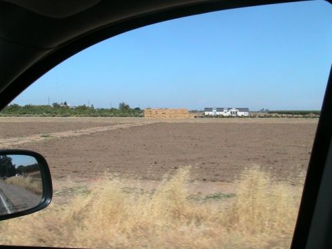 1971 Ford Bronco - View from a vehicle's side mirror shows a rural landscape with a field, hay bales, and a house under a clear blue sky.