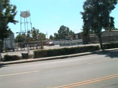 1971 Ford Bronco - A red car is parked in a lot next to a water tower, with a sign indicating biodiesel is sold there.