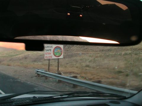 1971 Ford Bronco - View from inside a vehicle shows a road sign reflected in the rearview mirror, reminding drivers to 'DRIVE SAFE STAY ALIVE'.