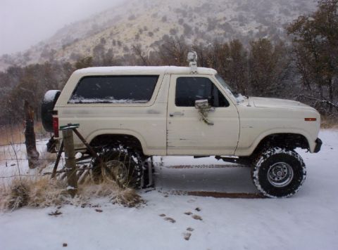 1983 Ford Bronco - White Ford Bronco with lifted suspension and spare tire on rear, parked in snow.