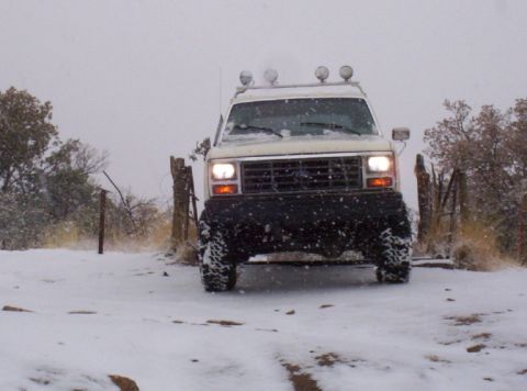 1983 Ford Bronco - A white SUV navigates a snowy landscape, its headlights illuminating the winter scene.